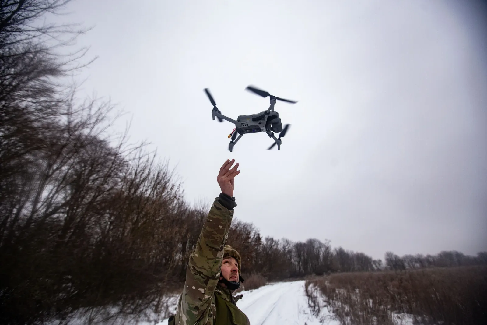 Un bărbat lansează o dronă într-un peisaj de iarnă, înconjurat de copaci.
