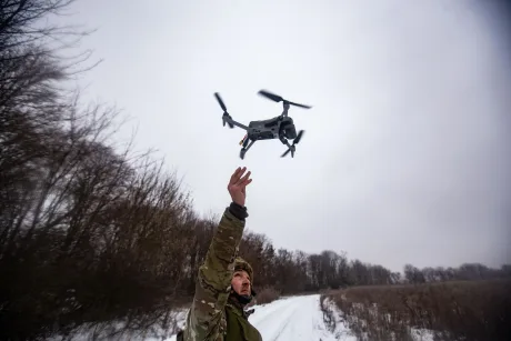 Un bărbat lansează o dronă într-un peisaj de iarnă, înconjurat de copaci.
