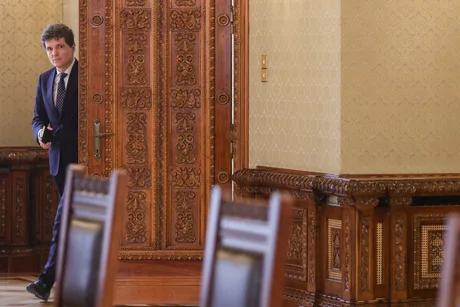 Un politician intrând într-o sală elegantă, cu uși din lemn sculptat.