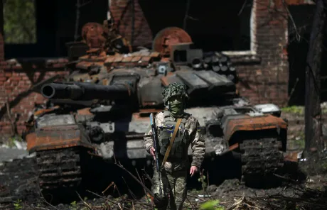 Soldat în fața unui tanc distrus în Ucraina, simbol al conflictului actual.