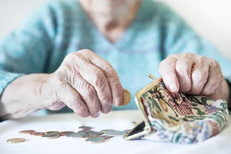 O persoană în vârstă numără monede dintr-un portofel pe masă.