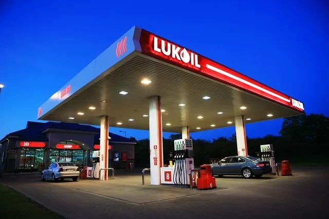 Stație de alimentare Lukoil iluminată noaptea, cu mașini parcate.