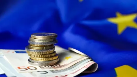Monede și bancnote euro pe fundalul steagului Uniunii Europene.