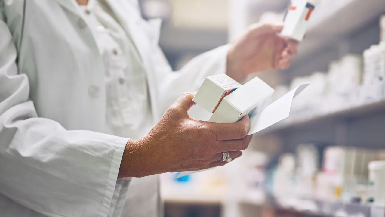 Un farmacist analizează cutii de medicamente într-o farmacie.