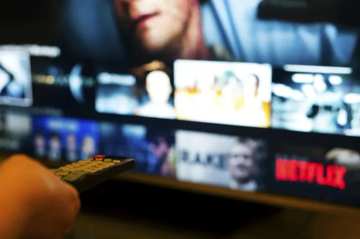 O persoană ținând o telecomandă în fața unui televizor cu Netflix.