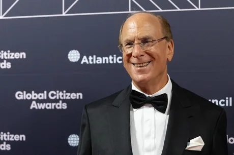 Larry Fink zâmbind la un eveniment, îmbrăcat elegant, cu un fundal sofisticat.