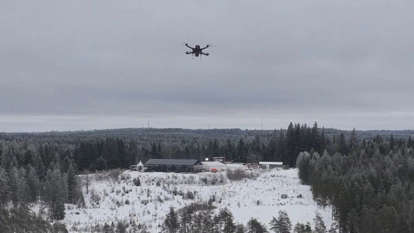 Dronă autonomă zburând deasupra unui peisaj de iarnă cu pădure și clădiri.