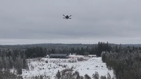 Dronă autonomă zburând deasupra unui peisaj de iarnă cu pădure și clădiri.