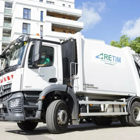 Autovehicul de salubritate RETIM parcând lângă un bloc de apartamente modern.