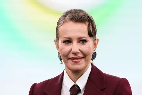 Ksenia Sobchak într-o ținută elegantă, zâmbind pe un fundal colorat.