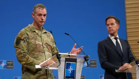 Un elicopter pe un vas, cu peisaj montan în fundal.