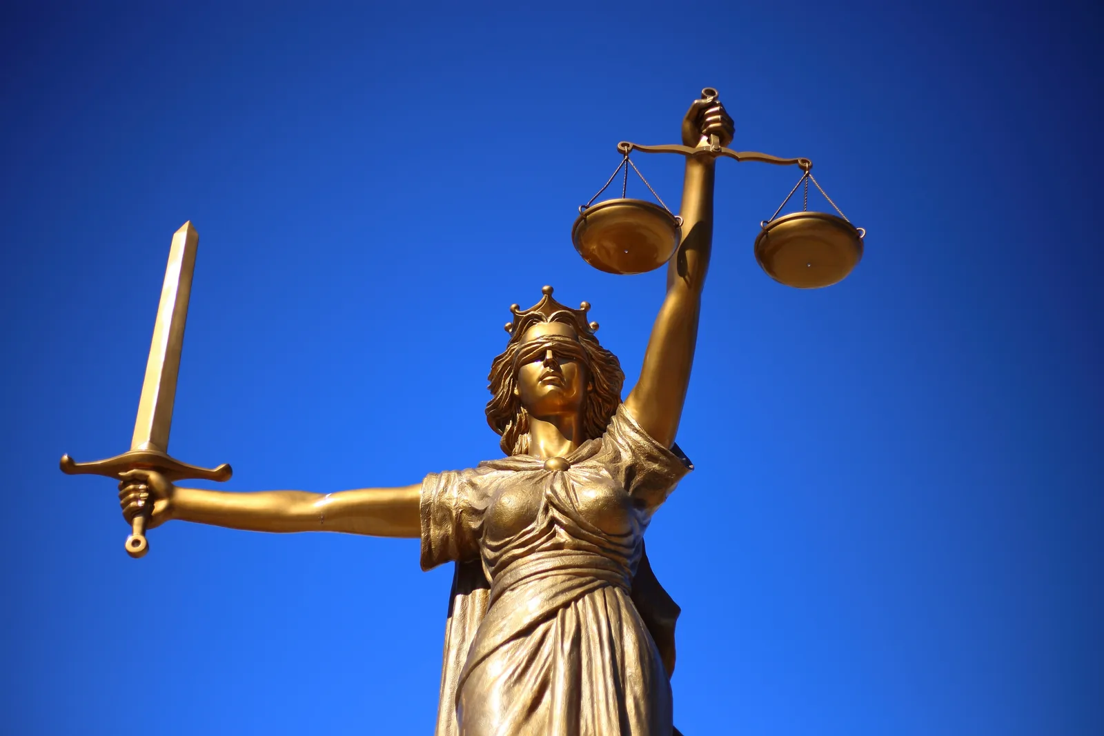 Statui simbolizând justiția, cu balanța și sabia, sub un cer senin.