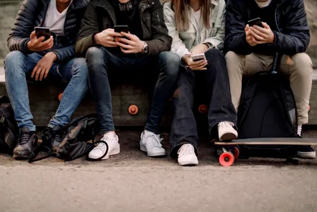 Tineri folosind telefoane mobile pe o bancă în parc.