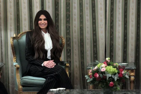 Kimberly Guilfoyle într-o întâlnire oficială, cu un buchet de flori pe masă.