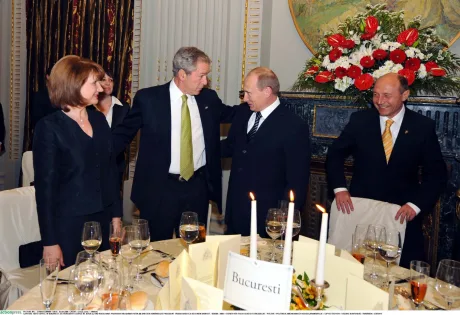 George Bush și Vladimir Putin discutând la o masă elegantă.