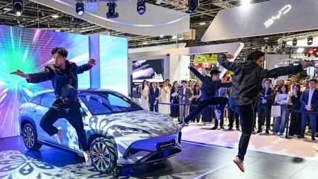 Dansatori performează lângă un vehicul electric pe un fundal vibrant.