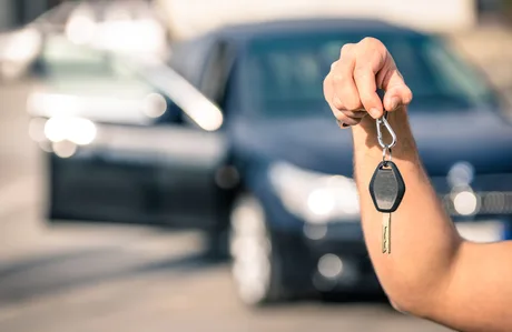 Cheie de mașină ținută de o persoană lângă un autoturism.