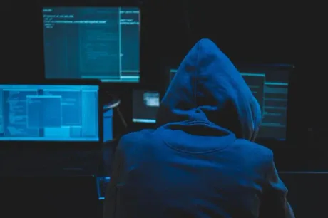 Un hacker lucrează la un computer în întuneric, evidențiind riscurile cibernetice.