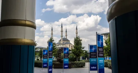 Bannere NATO în Ankara, cu moscheea în fundal, sub un cer senin.