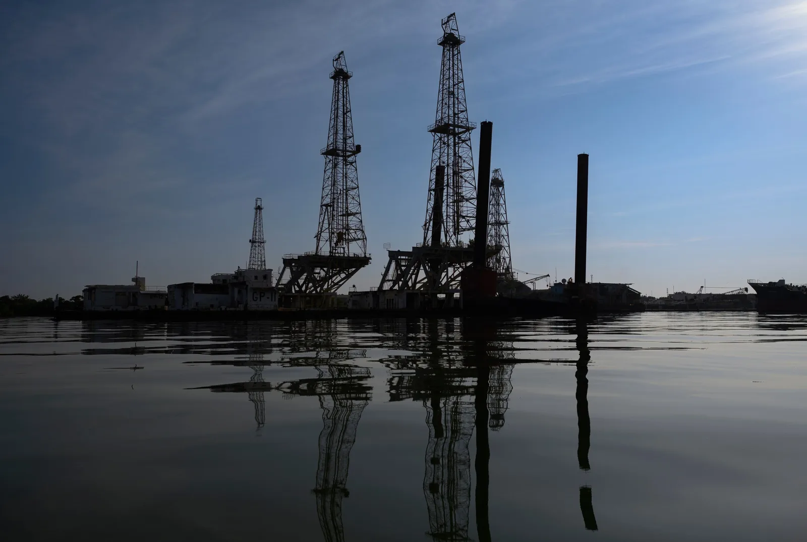 Platforme de extracție petrolieră reflectate în apă, sub un cer senin.