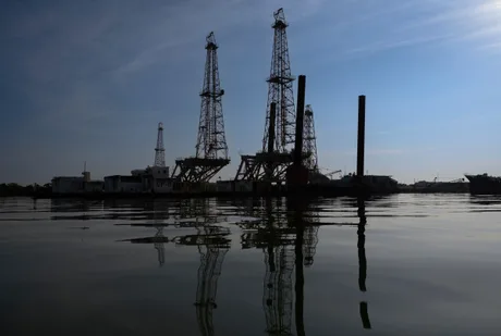 Platforme de extracție petrolieră reflectate în apă, sub un cer senin.