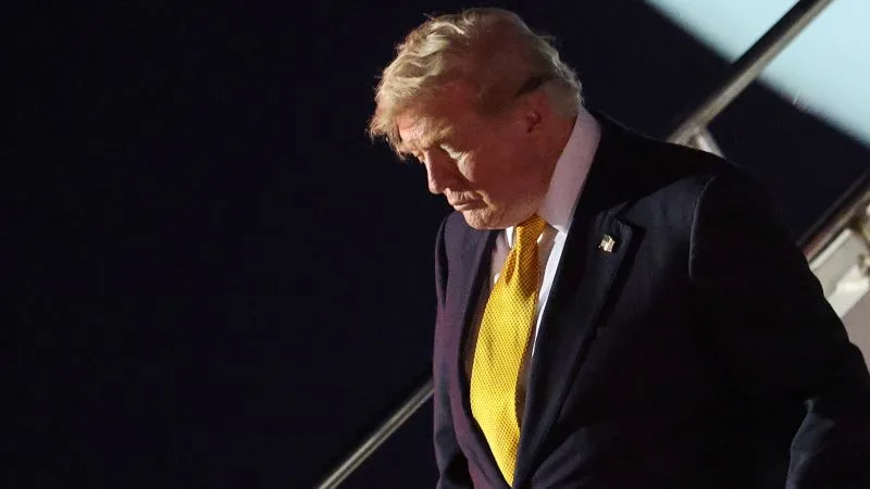 Donald Trump coborând dintr-un avion, cu o expresie serioasă pe față.