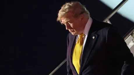 Donald Trump coborând dintr-un avion, cu o expresie serioasă pe față.