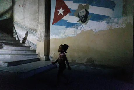 O fetiță merge pe scări, cu un mural al lui Fidel Castro în fundal.