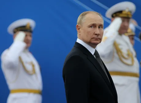 Putin în costum, cu soldați în fundal, privind serios.