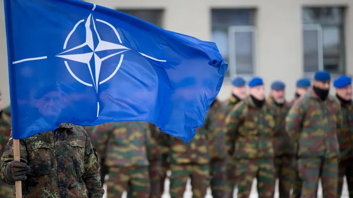 Soldați NATO în fața unei clădiri, cu steagul alianței fluturând.