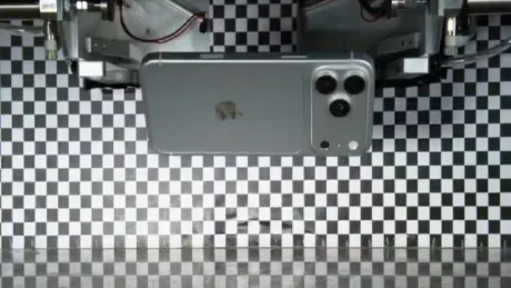 Un telefon iPhone pe un suport, cu un fundal în carouri alb-negru.