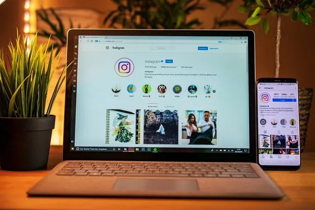 Ecran de laptop și telefon cu aplicația Instagram deschisă, pe un birou.