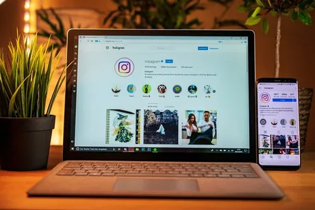 Ecran de laptop și telefon cu aplicația Instagram deschisă, pe un birou.