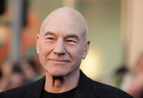 Patrick Stewart zâmbind, cu o expresie calmă și prietenoasă.
