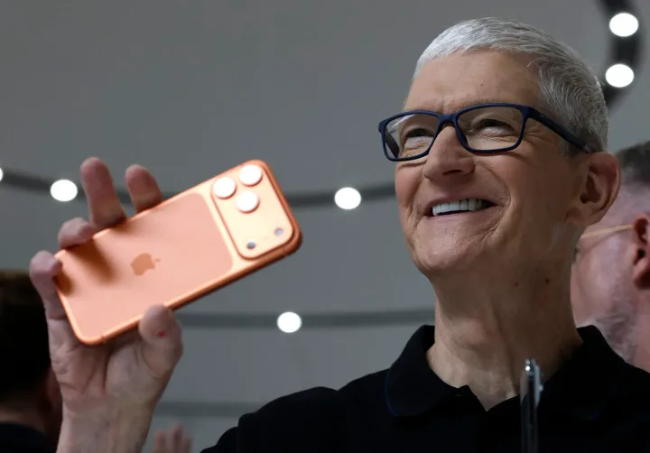 Tim Cook zâmbind în timp ce prezintă un nou model de iPhone.