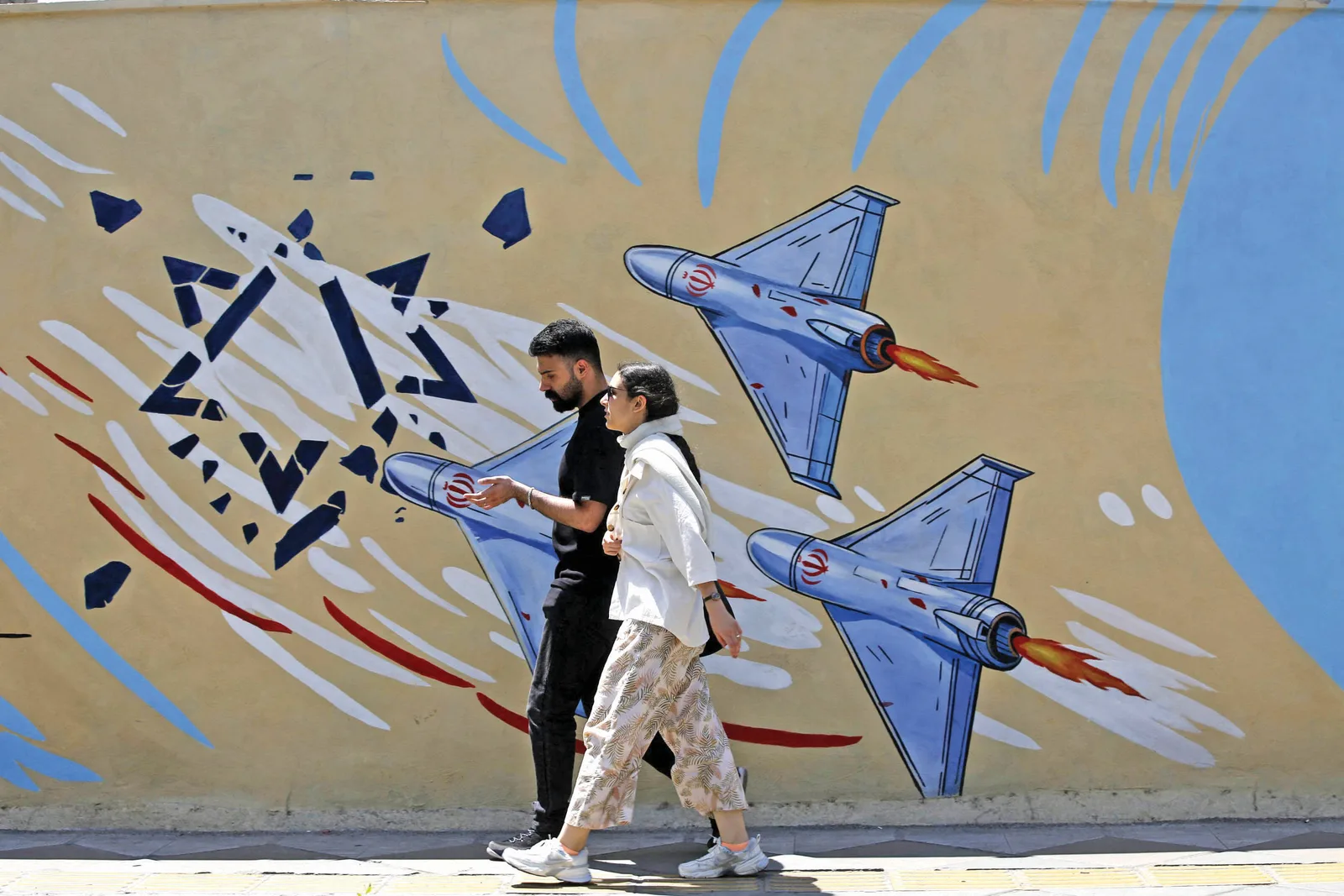 Oameni care trec pe lângă un mural cu avioane și simboluri ale conflictului.