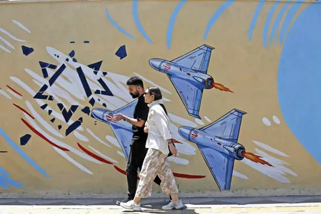 Oameni care trec pe lângă un mural cu avioane și simboluri ale conflictului.