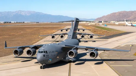 Avion militar C-17 Globemaster III pe pista de decolare, însoțit de munți în fundal.