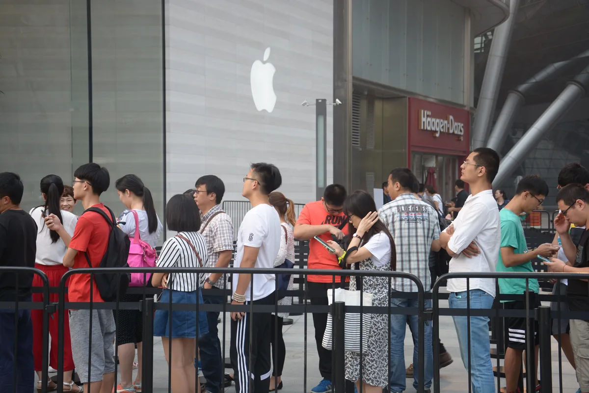 Oameni așteptând la o magazin Apple din China pentru a cumpăra smartphone-uri.