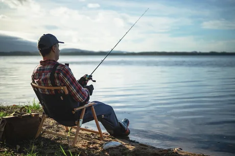Pescar relaxându-se pe malul unui lac, cu undița pregătită.