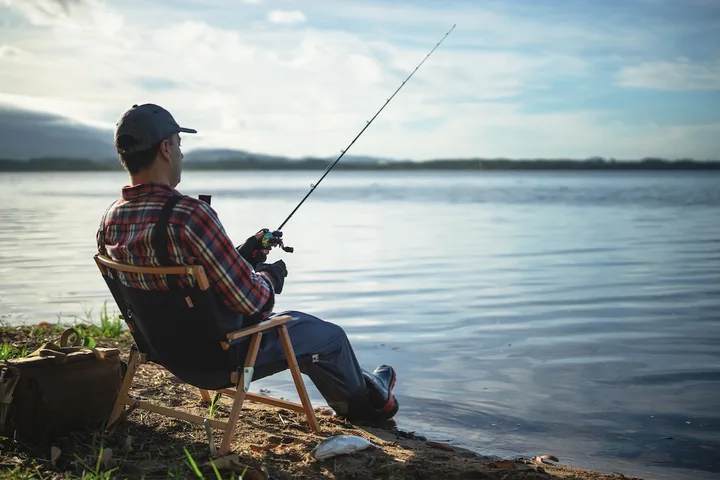 Pescar relaxându-se pe malul unui lac, cu undița pregătită.
