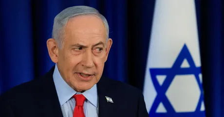 Benjamin Netanyahu discutând despre candidatură în fața steagului Israelului.