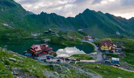 Peisaj montan cu pensiuni și lac în Munții Făgăraș, ideal pentru ecoturism.