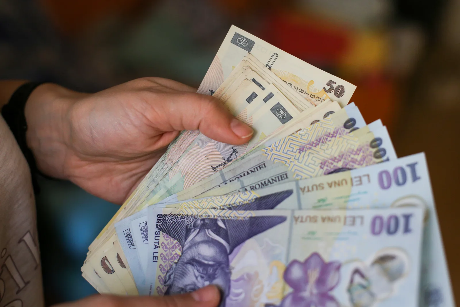 Bancnote românești în mână, simbolizând salariile din diverse județe.