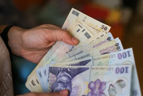 Bancnote românești în mână, simbolizând salariile din diverse județe.