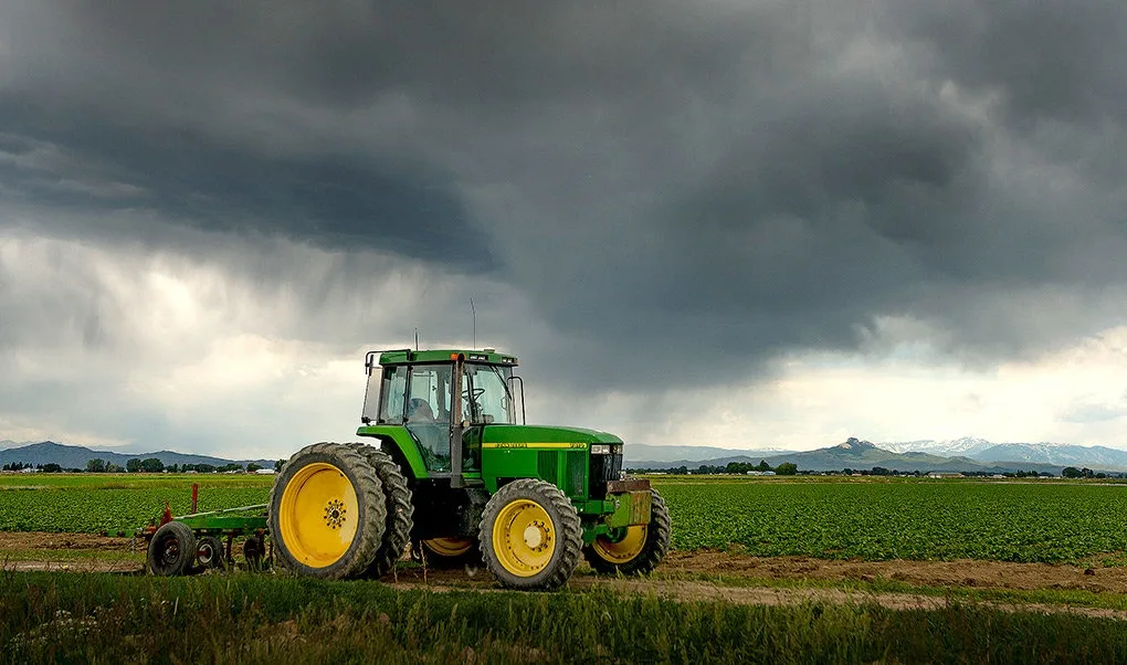 Tractor pe câmp sub nori întunecați, pregătit pentru lucrări agricole.