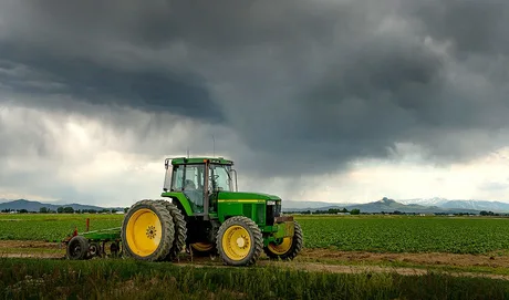 Tractor pe câmp sub nori întunecați, pregătit pentru lucrări agricole.