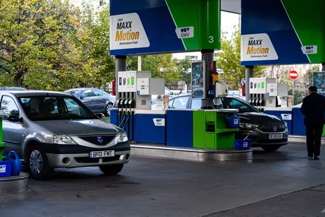 Stație de alimentare cu carburanți, mașini la pompă, peisaj urban.