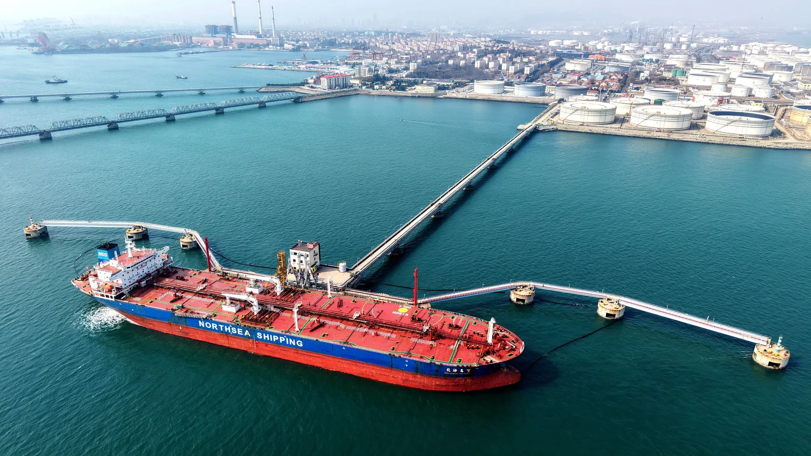 Vapor de transport maritim ancorat în port, cu rezervoare de petrol în fundal.