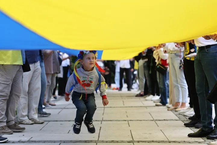 Un copil sărind sub un steag uriaș al Ucrainei, înconjurat de oameni.